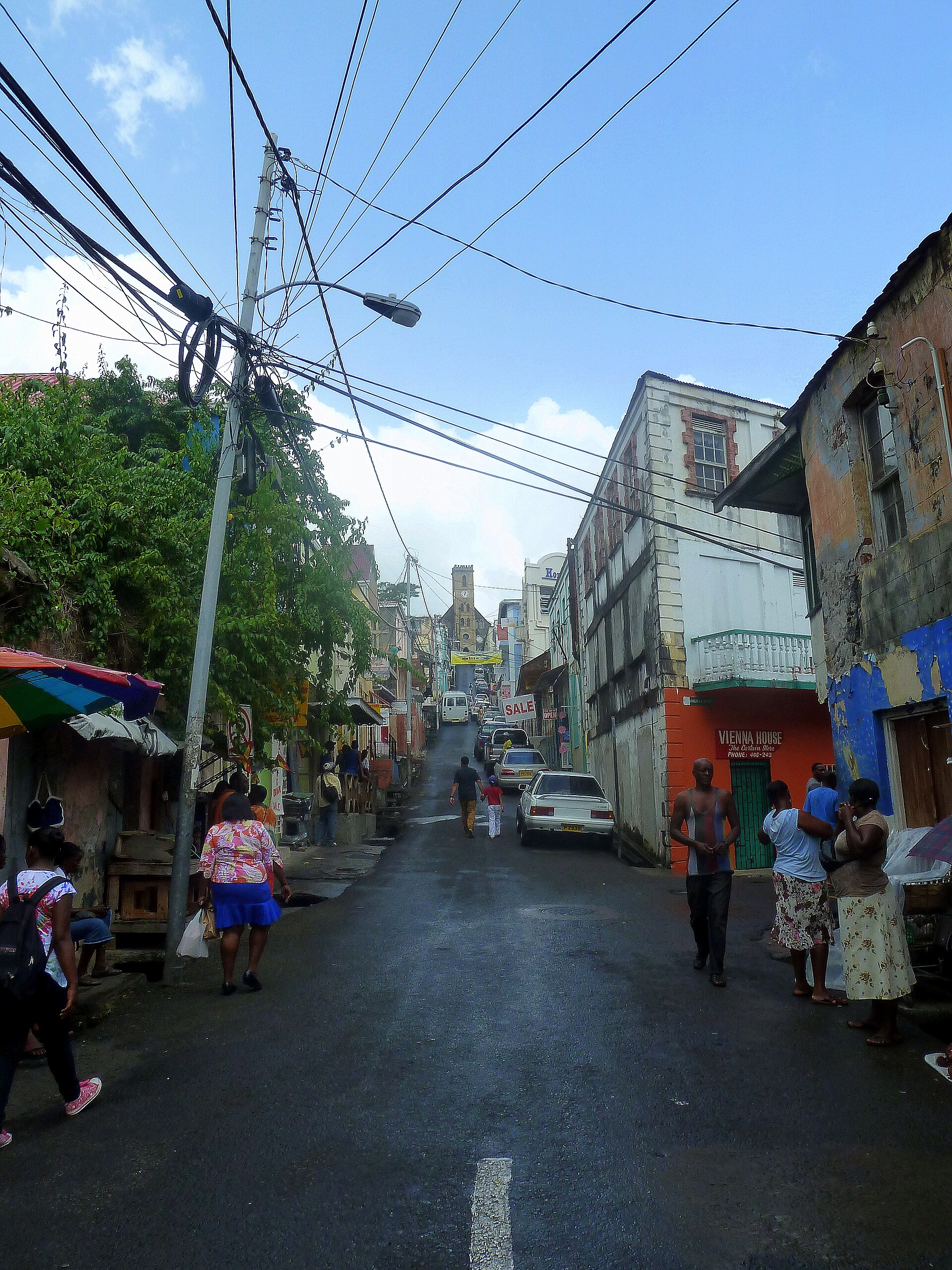 People walking along St. Juilles Street in St. George's, Grenada, with shops and overhead wires