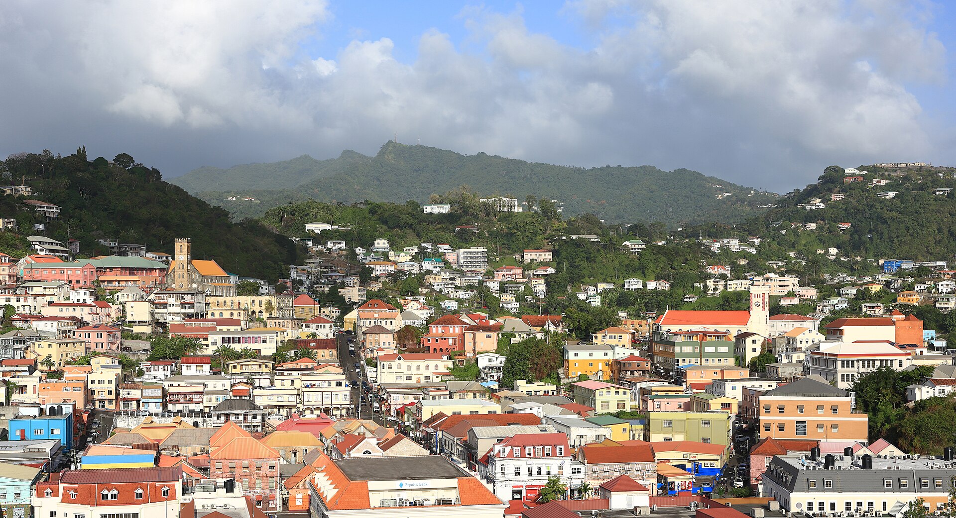 St. George's, Grenada, seen from above, with houses climbing the steep hillside and mountains rising behind the town